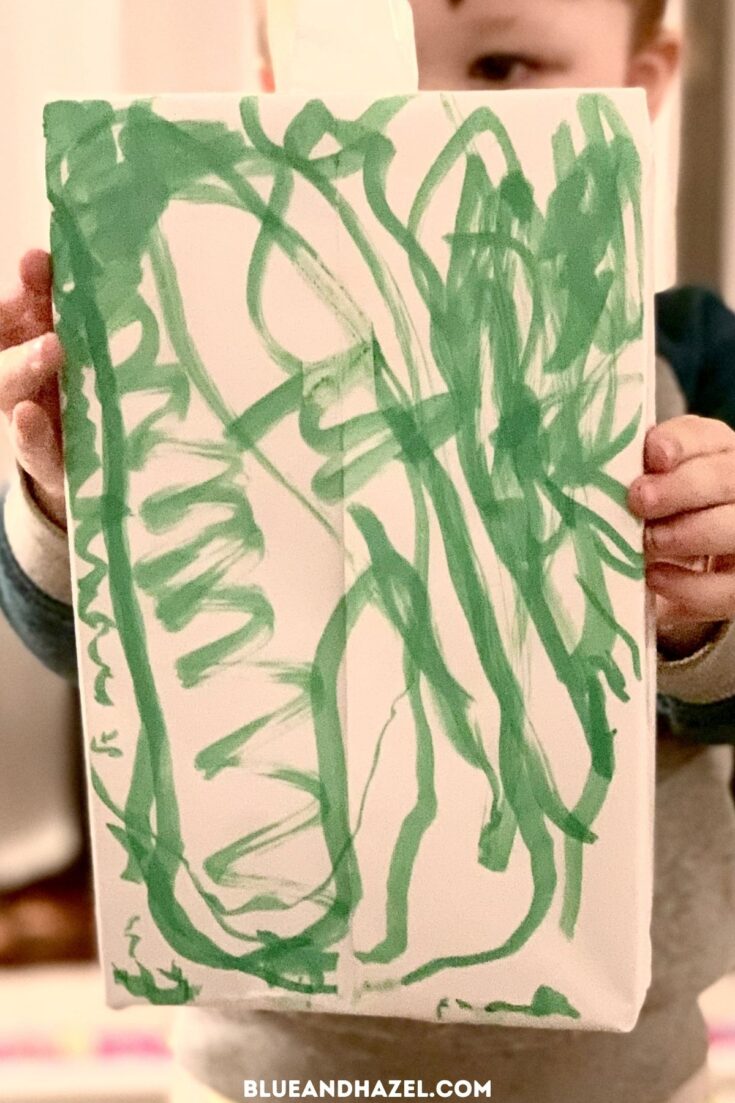 A present wrapped in white wrapping paper and scribbled on with a green marker by a toddler. 