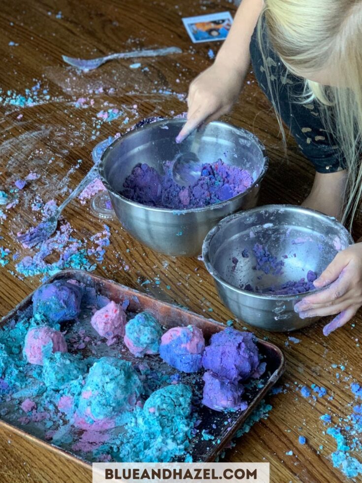 purple and blue moon sand formed into balls inside of a pan, with crumbly mess all over the floor.