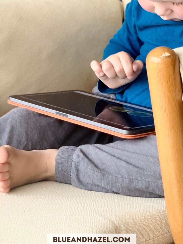 A toddler watching a show on an iPad in a chair. 