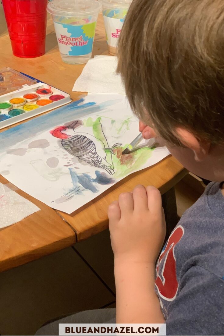 a 4 year old using watercolor paint to paint a red headed woodpecker. 