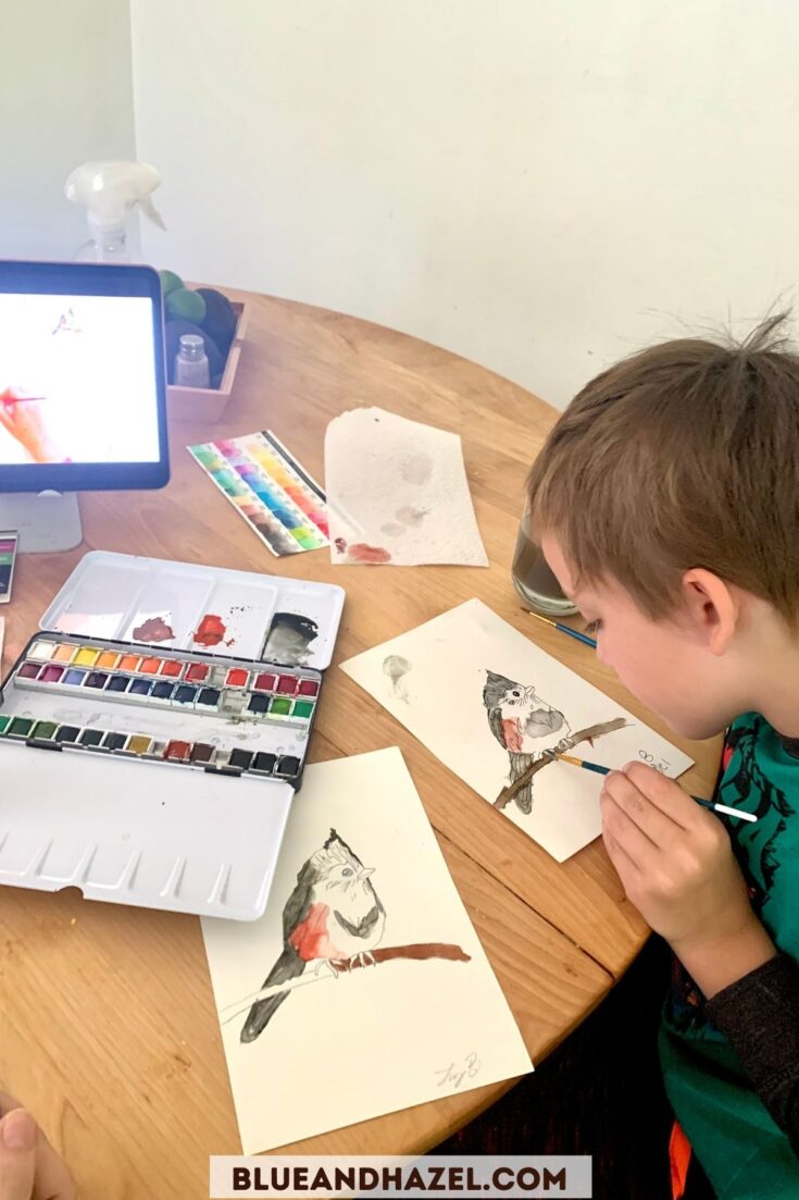 A 2nd grade boy watercolor painting a bird at the table using an ipad to watch the tutorial. 