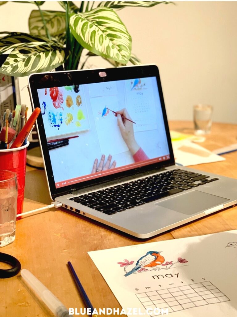 A Mac computer open with a watercolor tutorial on the screen and a picture of a bird being painted. 