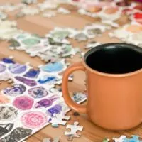 A coffee mug on a table with a puzzle of gemstones in progress