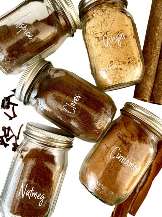 jars of ginger, cloves, allspice, cinnamon and nutmeg with a white background