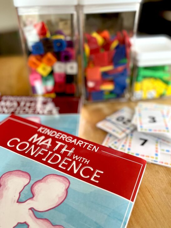 Kindergarten math with confidence student book on a table with math cubes and tangrams