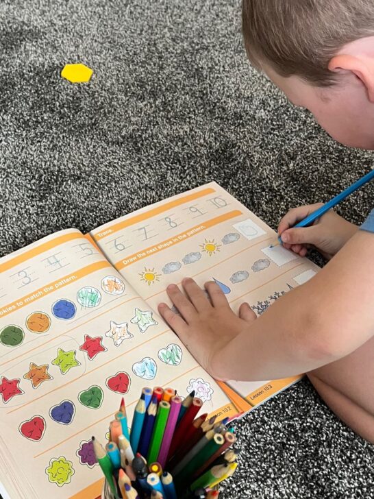 A 5.5 year old boy filling out patterns in his math workbook from kindergarten math with confidence.
