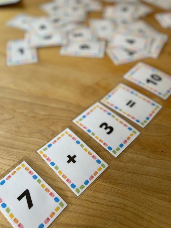 Laminated cards on a wooden table making a math equation saying 7+3=10.