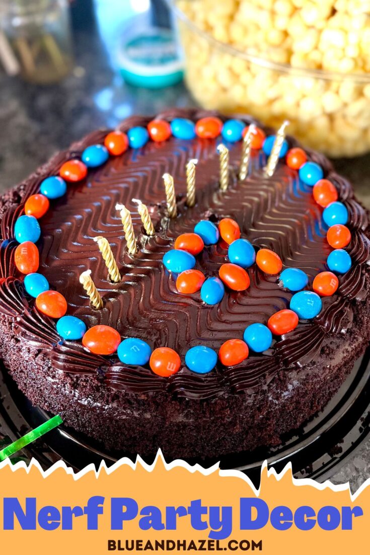 Round dark chocolate cake from Costco decorated by hand with orange and blue M and M's around the edge and 9 gold candles for a 9 year old's Nerf Party. 