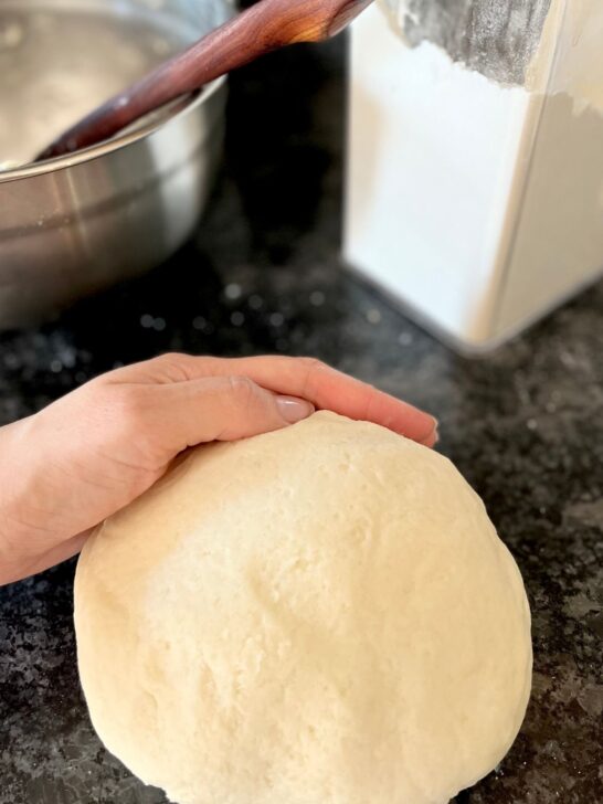 big ball of freshly made homemade white play dough with a hand touching it.