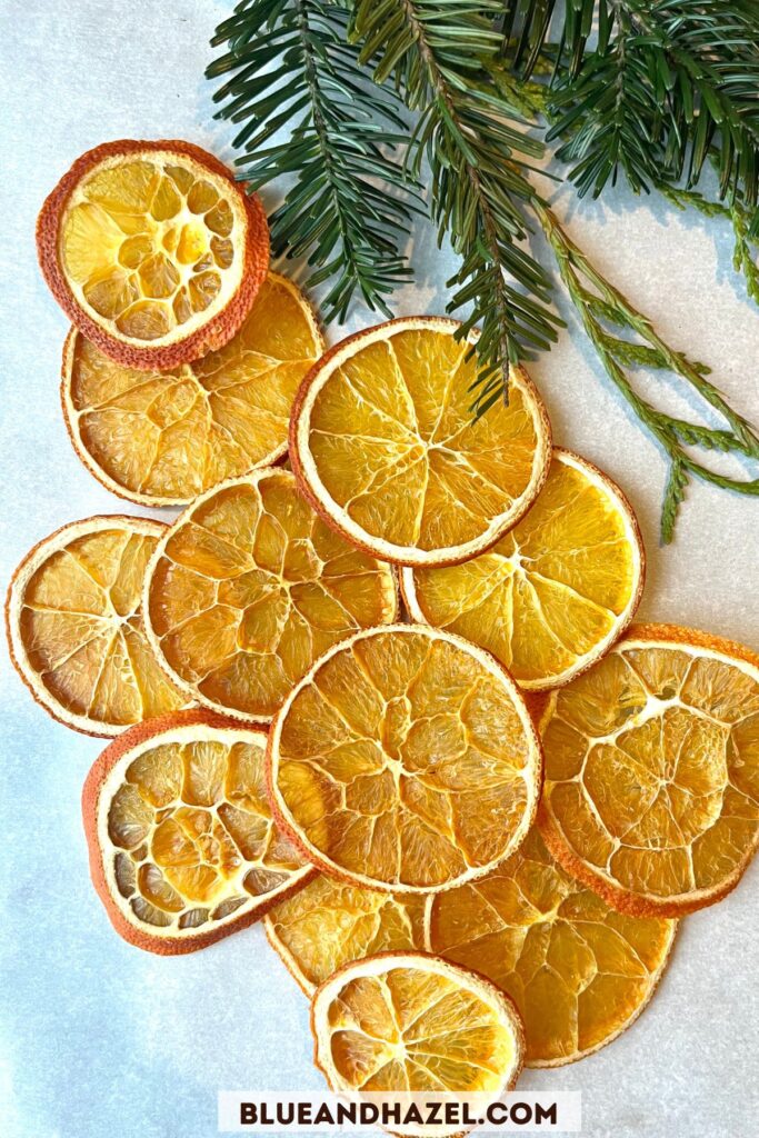 Beautiful bright dried orange slices piled on a white surface with pine laying next to the orange slices. 