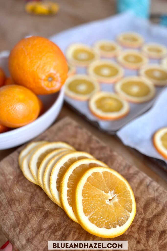 Orange slices on a cutting board with a baking sheet in the background for drying oranges in the oven. 