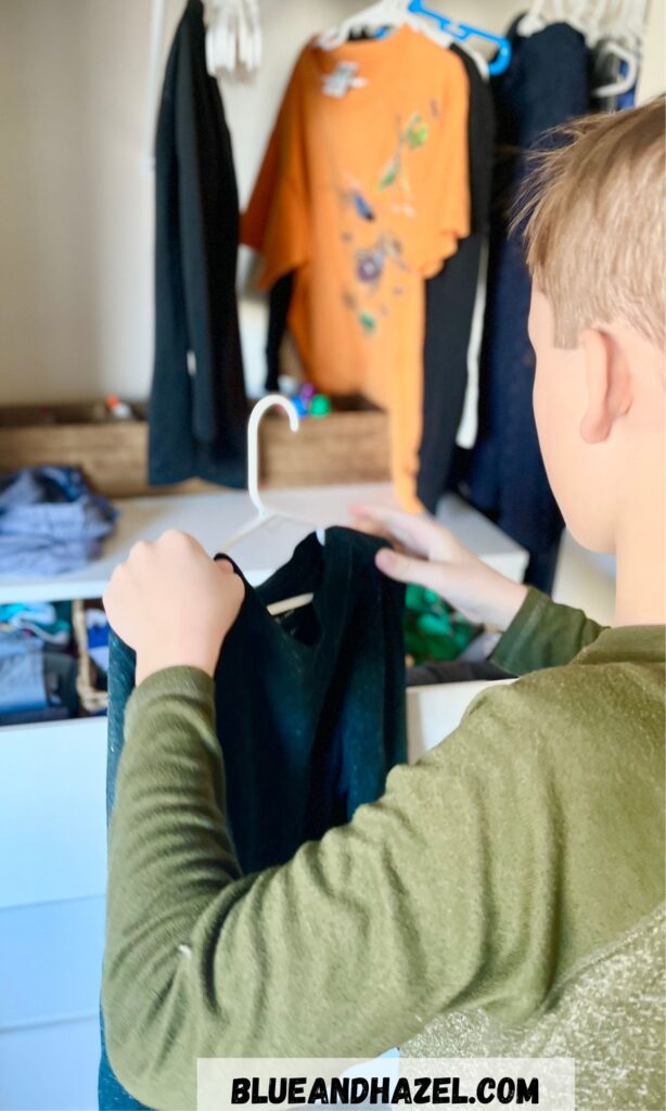 A 9 year old hanging up a shirt on a hanger during chore time.