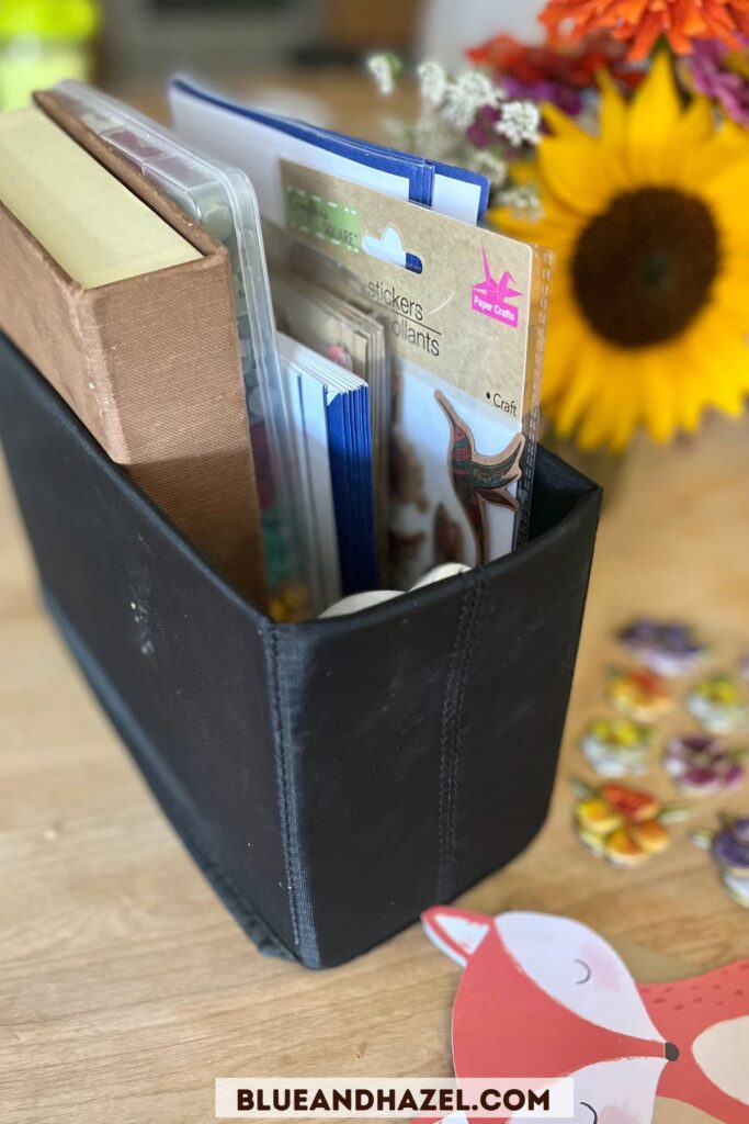 An upright black organizer for holding letter writing materials like envelopes, stamps, wax seal kit, and stickers. 
