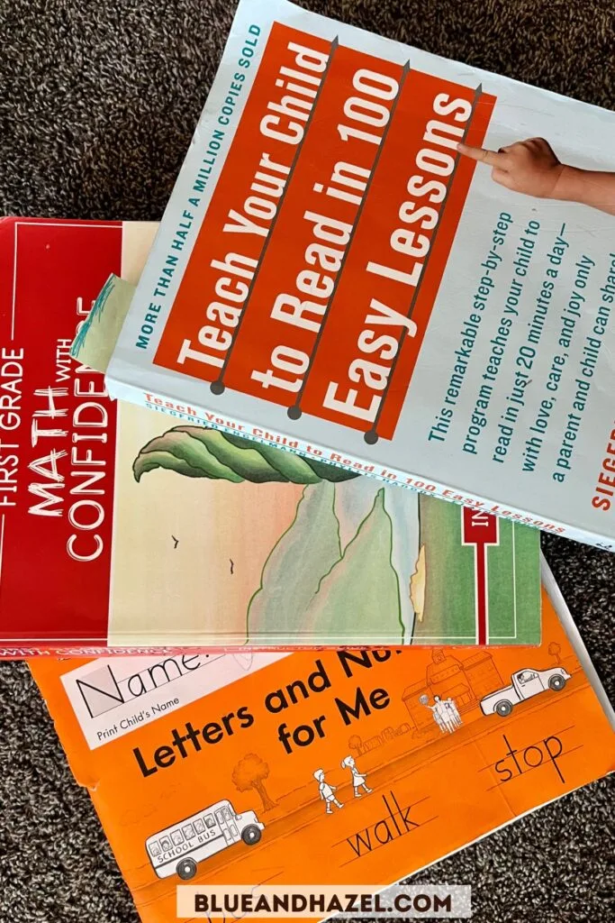 Teach Your Child To Read In 100 Easy Lessons, First Grade Math With Confidence, and Handwriting Without Tears books next to each other on the carpet. 