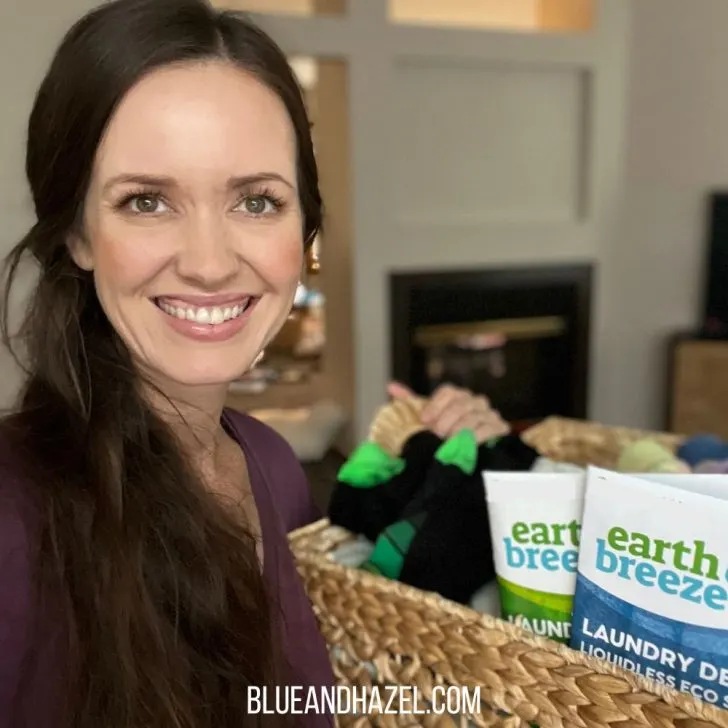 A homeschool mom holding a laundry basket and Earth Breeze laundry detergent eco sheets inside. 